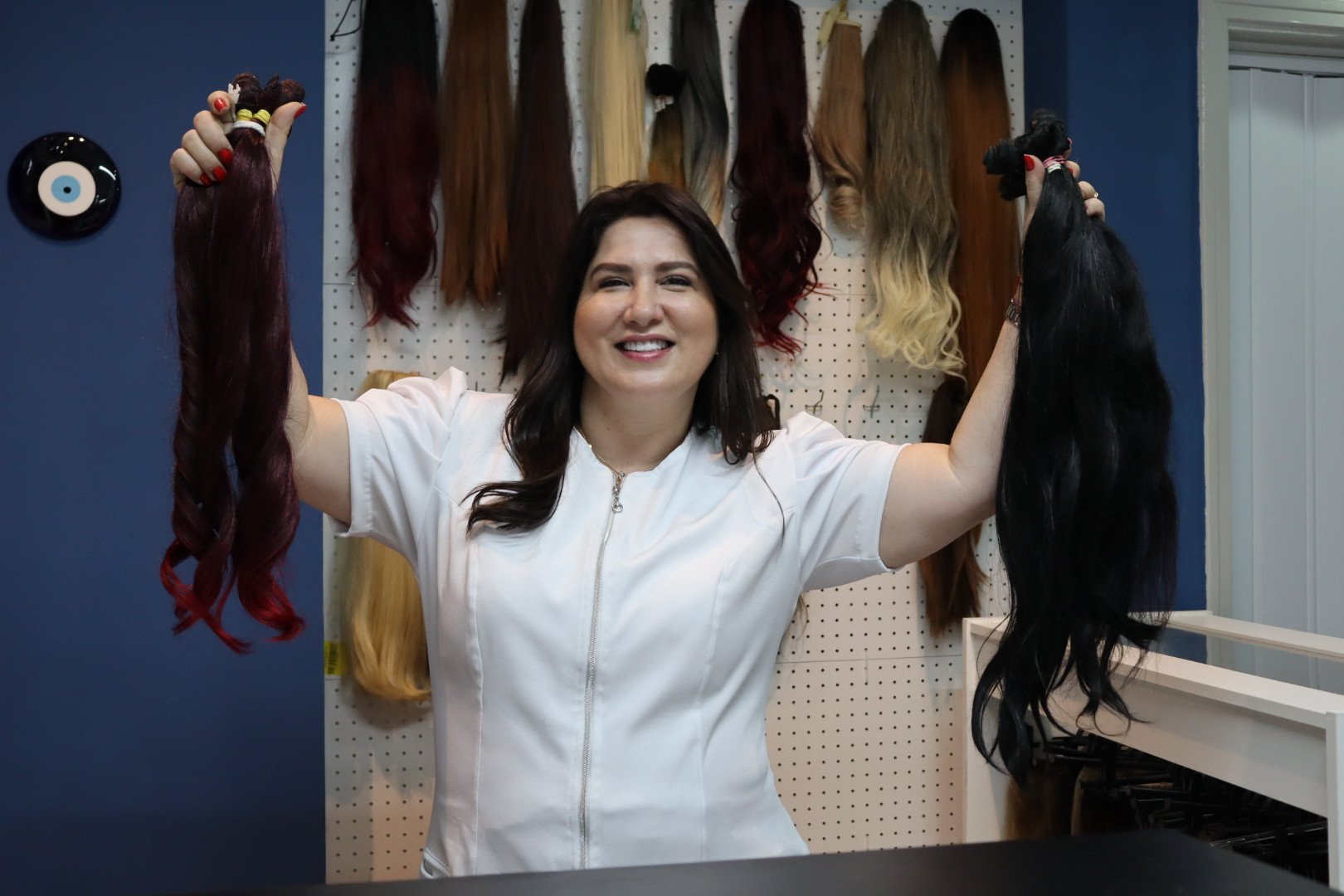 Cristina Orosa segurando mechas naturais coloridas em frente ao painel de produtos